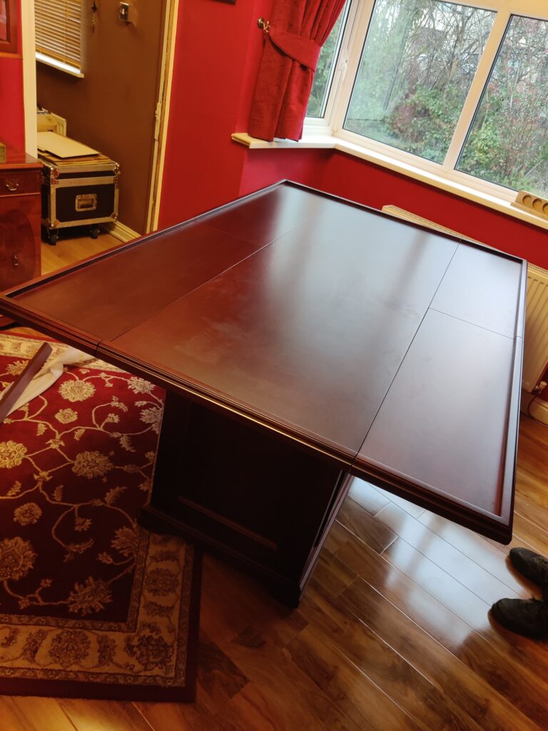 This bespoke gaming table was designed and crafted to deliver total functionality within a compact living space, without compromising on style. Positioned within a bay window, the brief was to create a table that could remain neatly tucked away for everyday use… Yet transform effortlessly into a full-sized gaming surface when required. The solution was a cleverly engineered drop-leaf design, allowing the table to sit compactly into the bay window area before expanding to a generous 6ft x 4ft playing surface. This provides ample space for board games, cards, and Warhammer type games, all while maintaining a clean and unobtrusive footprint when not in use. Mobility was a key consideration. The table is mounted on four heavy-duty locking castors, enabling it to be moved with ease and securely fixed in position once in place. This flexibility ensures the table can adapt to the room as needed, whether for entertaining or everyday living. Internally, the cabinet features bifold doors in front of adjustable shelves, offering practical storage for games and accessories while maintaining a refined exterior appearance. High-quality hardware, including folding table hinges and precision joinery, ensures smooth operation and long-term durability. Crafted using mahogany veneered MDF with solid mahogany mouldings, the table was finished with a stain and lacquer carefully selected to complement the client’s existing furniture. Traditional detailing, including decorative handles, ties the piece seamlessly into the room’s established aesthetic. The result is a highly versatile, beautifully crafted piece that balances practicality with timeless design a perfect example of bespoke furniture tailored to both space and lifestyle. If you’re considering a bespoke piece tailored to your space, explore more of our recent projects or get in touch to discuss your ideas. At JFW Cabinetmakers, we specialise in creating furniture that works beautifully for the way you live.
