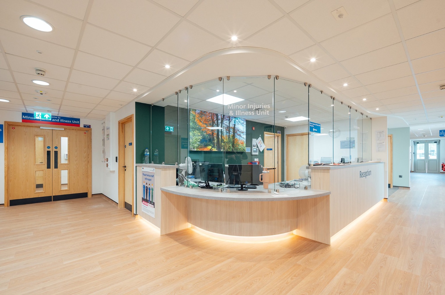 Curved timber reception desk with glazed screens and integrated lighting in a healthcare setting