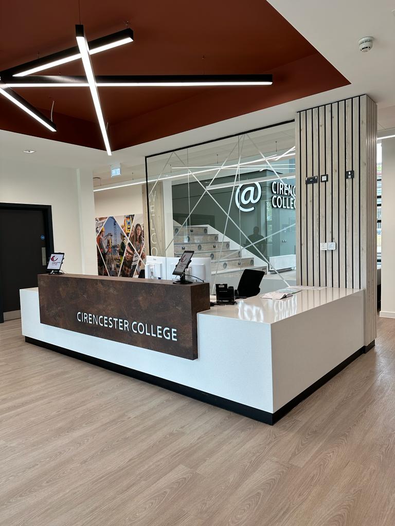 Bespoke reception desk with illuminated Cirencester College branding and slatted feature wall